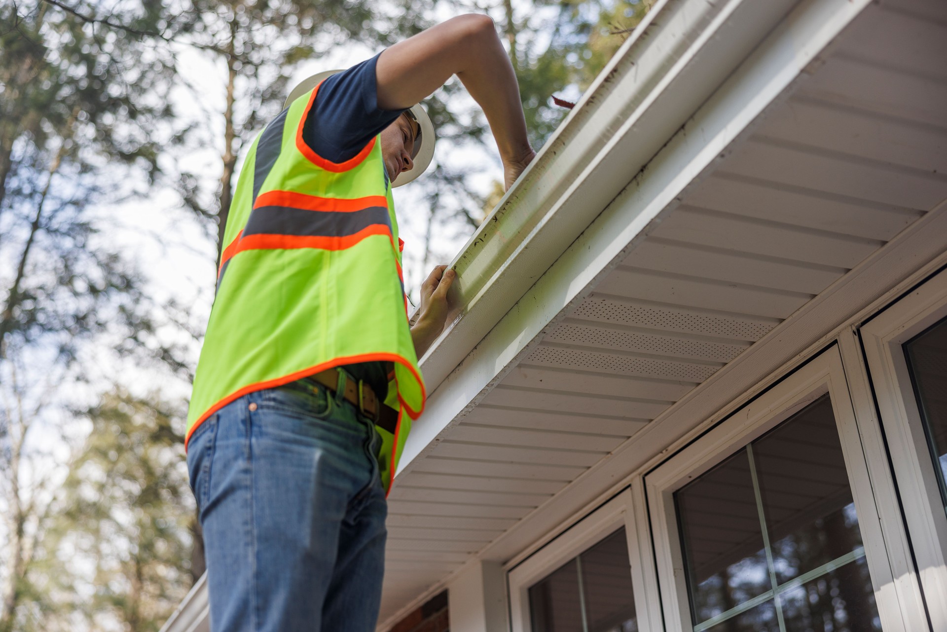 Blue collar worker outside  on a ladder cleaning the gutters of the house. Focus on the foreground with defocused background.